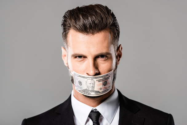 Ovela liikemies mustassa puvussa dollarin seteli suussa eristetty harmaalla
 - Valokuva, kuva