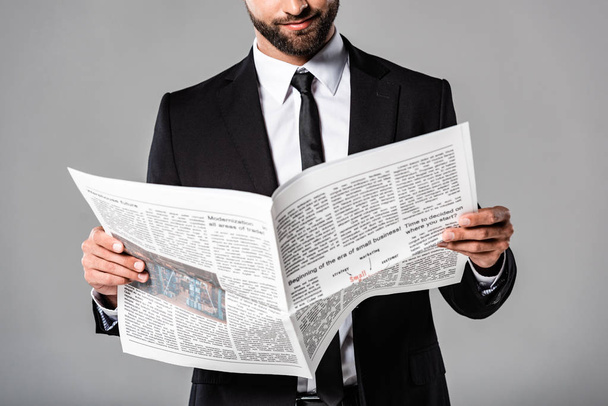 wykadrowany widok biznesmen w czarnym kolorze z gazetą wyizolowaną na szaro - Zdjęcie, obraz