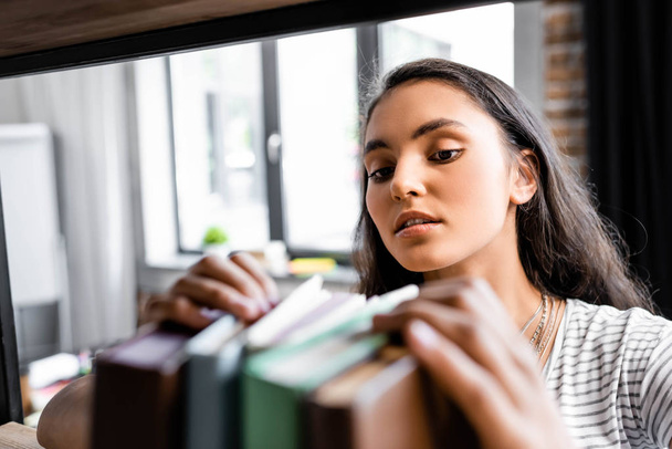 selective focus of bi-racial student holding books in apartment  - Foto, afbeelding