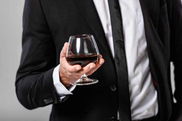 partial view of businessman in black suit holding glass with whiskey isolated on grey - Photo, Image