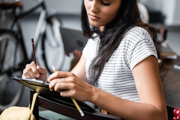 atraente e bi-racial estudante escrevendo com lápis no apartamento
  - Foto, Imagem