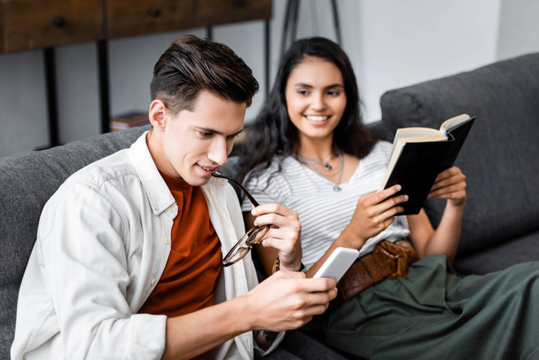 étudiants multiculturels tenant un livre et utilisant un smartphone dans l'appartement
  - Photo, image