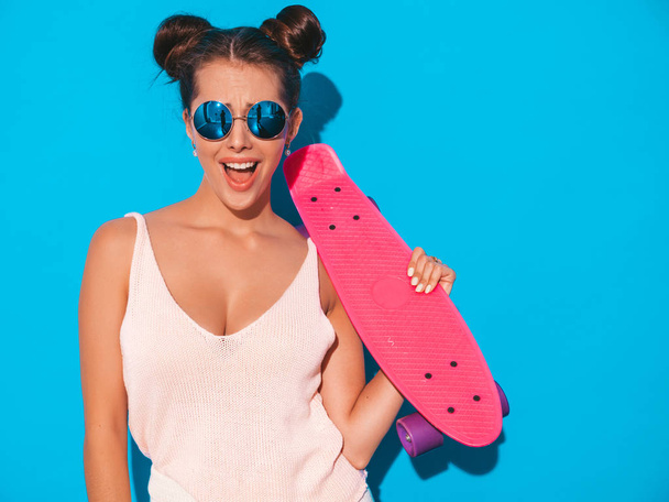 Young beautiful sexy smiling hipster woman in sunglasses.Trendy girl in summer knitted cardigan topic ,shorts.Positive female going crazy with pink penny skateboard,isolated on - Photo, image