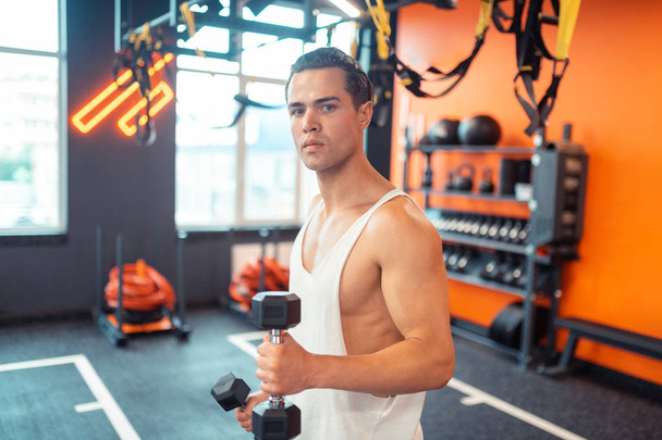Nice attractive sportsman standing with a dumbbell - Fotó, kép