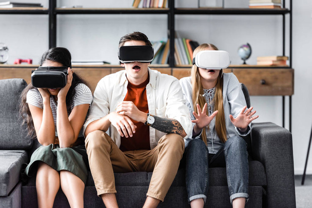 потрясенные мультикультурные друзья с наушниками виртуальной реальности, сидящие на диване
  - Фото, изображение