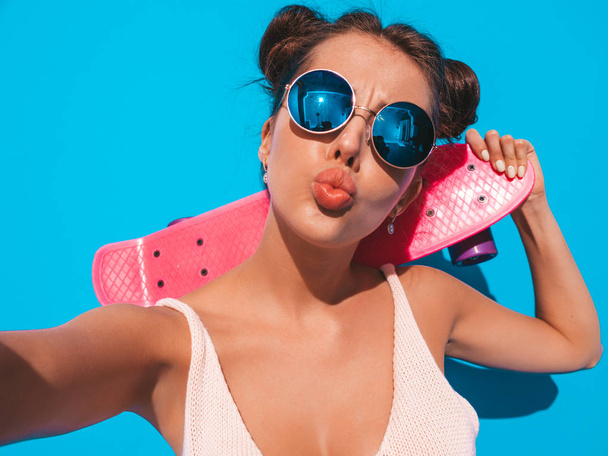 Young beautiful sexy smiling hipster woman in sunglasses.Trendy girl in summer knitted cardigan.Female with pink penny skateboard,isolated on - Фото, изображение