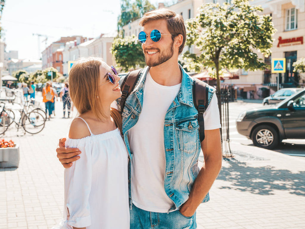 Smiling beautiful girl and her handsome boyfriend posing in the street. Woman in casual summer dress and man in jeans clothes. Happy cheerful couple family having fun in sunglasses - Fotoğraf, Görsel