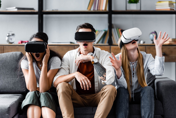 multicultural friends with virtual reality headsets sitting on sofa  - Foto, Imagen