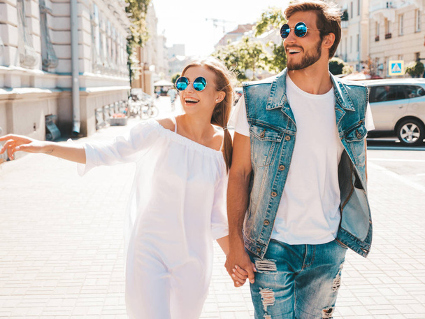 Smiling beautiful girl and her handsome boyfriend posing in the street. Woman in casual summer dress and man in jeans clothes. Happy cheerful couple family having fun in sunglasses - Фото, зображення