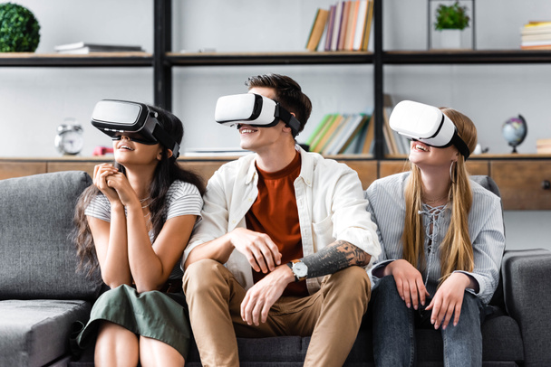 smiling multicultural friends with virtual reality headsets sitting on sofa  - Fotografie, Obrázek