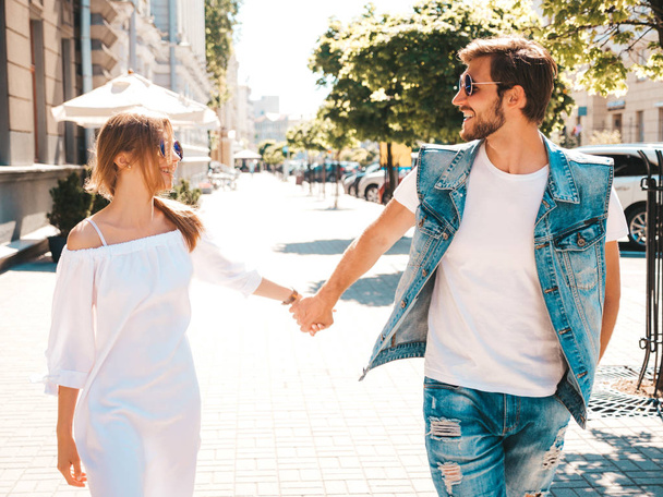 Smiling beautiful girl and her handsome boyfriend posing in the street. Woman in casual summer dress and man in jeans clothes. Happy cheerful couple family having fun in sunglasses - Zdjęcie, obraz