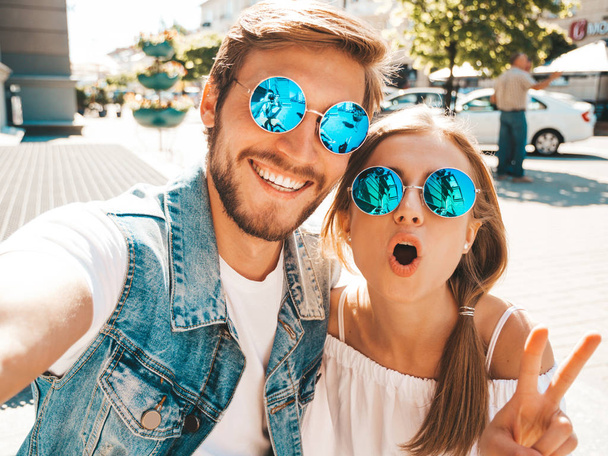 Smiling beautiful girl and her handsome boyfriend in casual summer clothes.Happy family taking selfie self portrait of themselves on smartphone camera in sunglasses.Having fun on the street background - 写真・画像