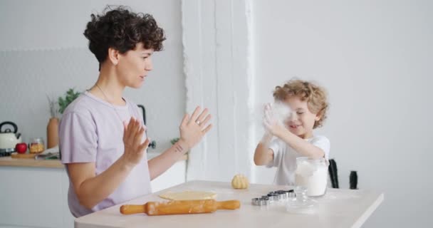 Happy child having fun with flour clapping hands cooking pastry with mom at home - Záběry, video