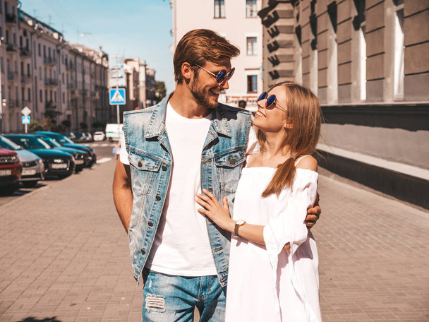 Smiling beautiful girl and her handsome boyfriend walking in the street. Woman in casual summer dress and man in jeans clothes. Happy cheerful couple family having fun in sunglasses - Valokuva, kuva