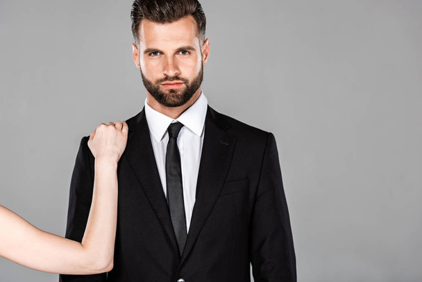 Frau berührt erfolgreichen Geschäftsmann im schwarzen Anzug isoliert auf grau - Foto, Bild