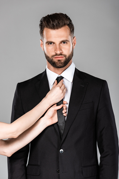 woman touching tie on confident businessman in black suit isolated on grey - Valokuva, kuva
