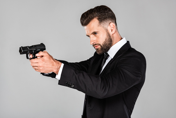 handsome agent in black suit aiming gun isolated on grey - Photo, Image