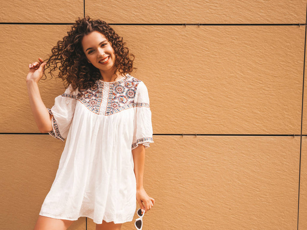 Beautiful smiling model with afro curls hairstyle dressed in summer hipster white dress.Sexy carefree girl posing in the street near yellow wall.Funny and positive woman having fun. - Photo, image