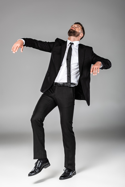 full length view of zombie businessman in black suit walking on grey - Fotó, kép