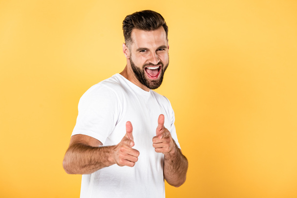 hombre guapo feliz en camiseta blanca apuntando con los dedos a la cámara aislada en amarillo
 - Foto, imagen