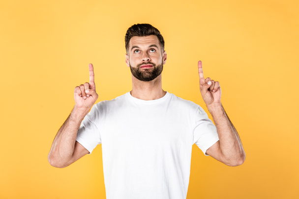 handsome man in white t-shirt pointing with fingers above isolated on yellow - Photo, Image