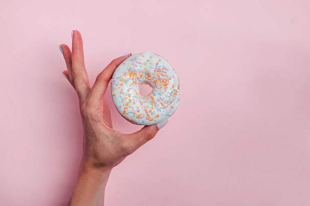 Womans hand holding a donut with colorful sprinkles on pink background - Foto, Bild