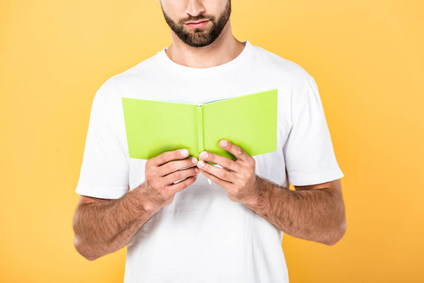 περικομμένη θέα του άντρα με γένια σε λευκό μπλουζάκι διαβάζοντας βιβλίο απομονωμένο σε κίτρινο - Φωτογραφία, εικόνα