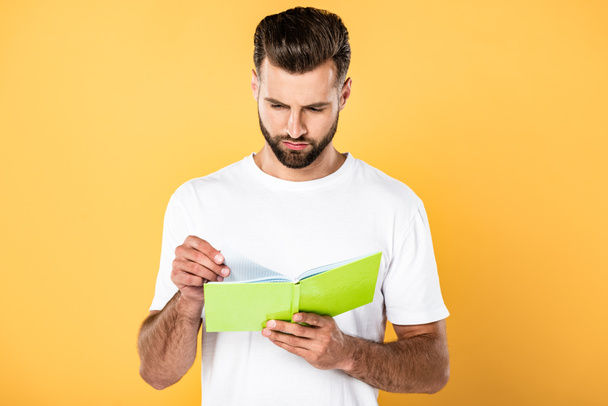 handsome man in white t-shirt reading book isolated on yellow - Photo, Image