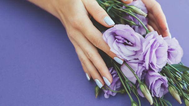 Purple manicure on a plain background with a flower. - Fotó, kép