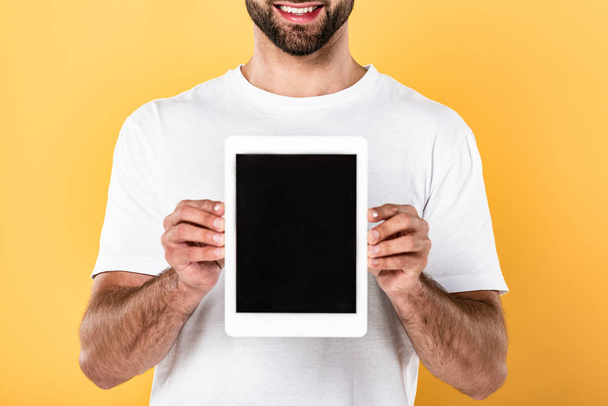 partial view of smiling man in white t-shirt showing digital tablet with blank screen isolated on yellow - Zdjęcie, obraz