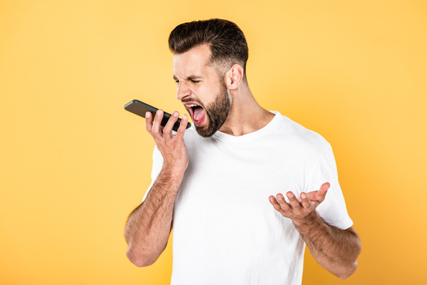 irritated man in white t-shirt screaming in smartphone isolated on yellow - Zdjęcie, obraz