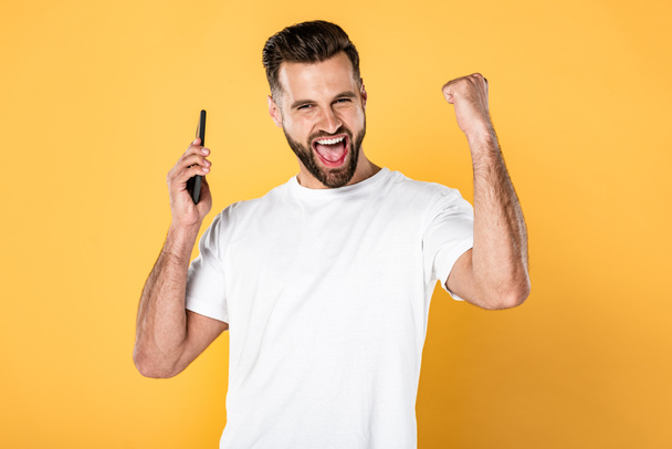 hombre feliz en camiseta blanca hablando en el teléfono inteligente y mostrando sí gesto aislado en amarillo
 - Foto, imagen
