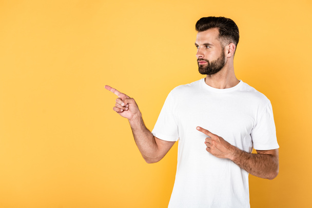 hombre guapo en camiseta blanca señalando con los dedos a un lado aislado en amarillo
 - Foto, imagen