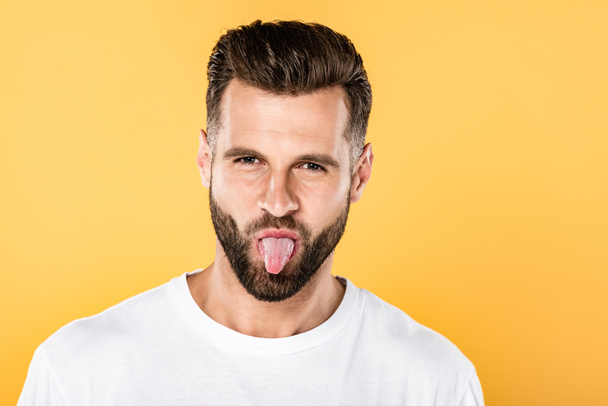 funny man in white t-shirt showing tongue isolated on yellow - Fotó, kép