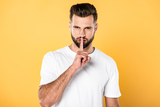 handsome man in white t-shirt showing shh sign isolated on yellow - Photo, Image