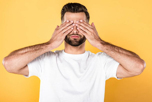 man in white t-shirt with hands on eyes isolated on yellow - Photo, image