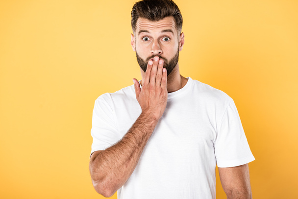 shocked handsome man in white t-shirt with hand on mouth isolated on yellow - Photo, Image