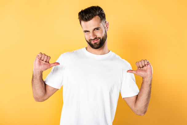 smiling handsome man in white t-shirt pointing with fingers at himself isolated on yellow - Fotografie, Obrázek