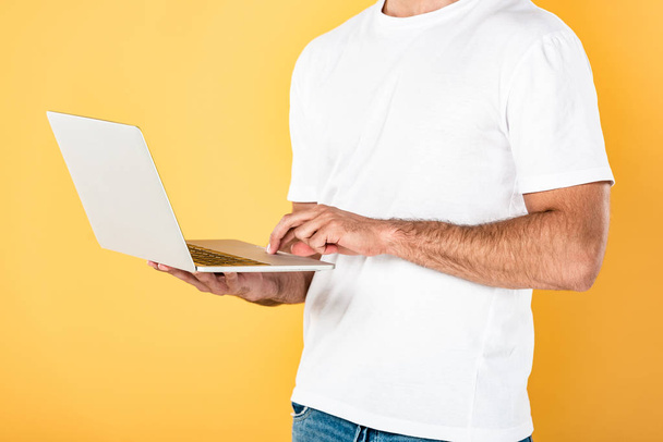 обрезанный вид человека в белой футболке с помощью ноутбука, изолированного на желтый
 - Фото, изображение