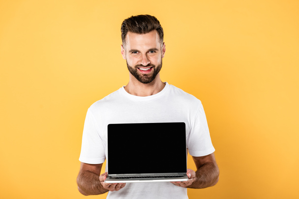 hombre guapo feliz en camiseta blanca que muestra el ordenador portátil con la pantalla en blanco aislado en amarillo
 - Foto, Imagen