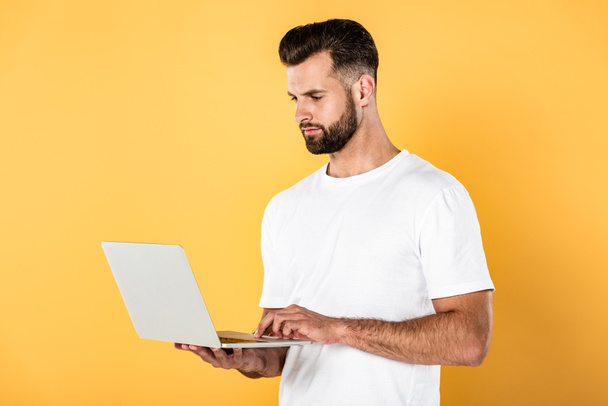 άντρας σε λευκό μπλουζάκι χρησιμοποιώντας φορητό υπολογιστή απομονωμένο σε κίτρινο - Φωτογραφία, εικόνα