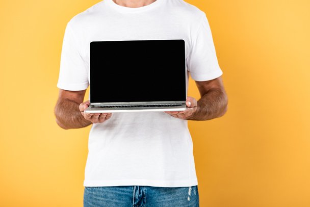 partial view of man in white t-shirt showing laptop with blank screen isolated on yellow - Zdjęcie, obraz