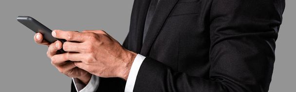 vista parcial del hombre de negocios en traje negro usando teléfono inteligente aislado en gris, plano panorámico
 - Foto, Imagen