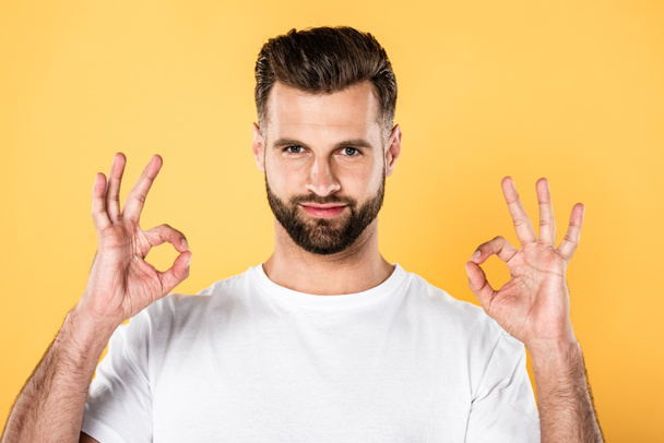 handsome man in white t-shirt showing okay signs isolated on yellow - Fotó, kép