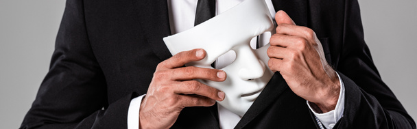 recortado vista de hombre de negocios en traje negro con máscara blanca aislado en gris, tiro panorámico
 - Foto, imagen