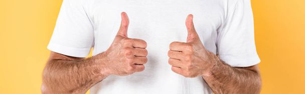 partial view of man in white t-shirt showing thumbs up isolated on yellow, panoramic shot - Foto, Imagen