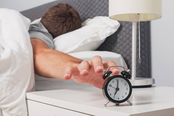 Mans hand reaching out alarm clock on the nightstand early in the morning. - Фото, зображення