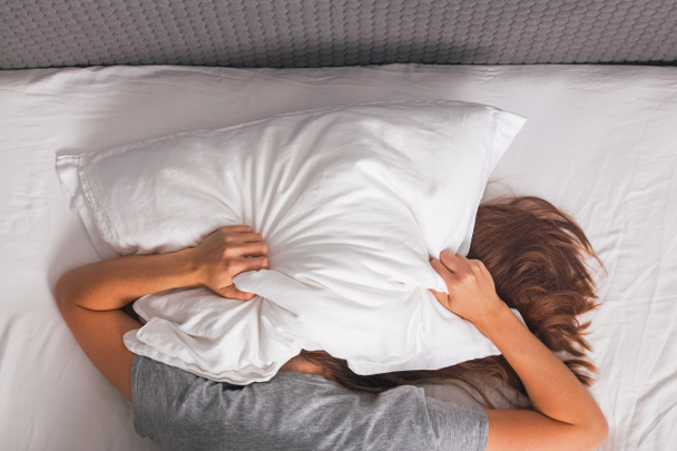 Жінка лежить у ліжку і покриває голову подушкою
. - Фото, зображення