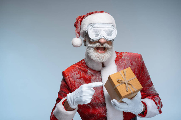 Санта-Клаус указывает на подарок на Новый год в руке
 - Фото, изображение