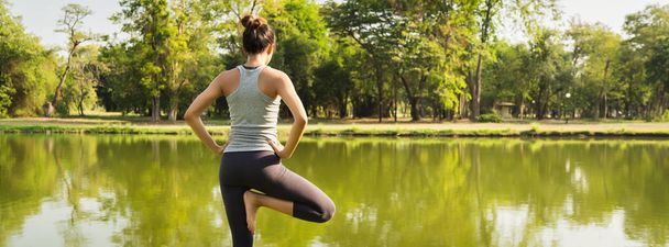Joven mujer asiática yoga al aire libre mantener la calma y medita mientras practica yoga para explorar la paz interior. El yoga tiene buenos beneficios para la salud cerca del lago en el parque. Fondo de la bandera panorámica
. - Foto, Imagen